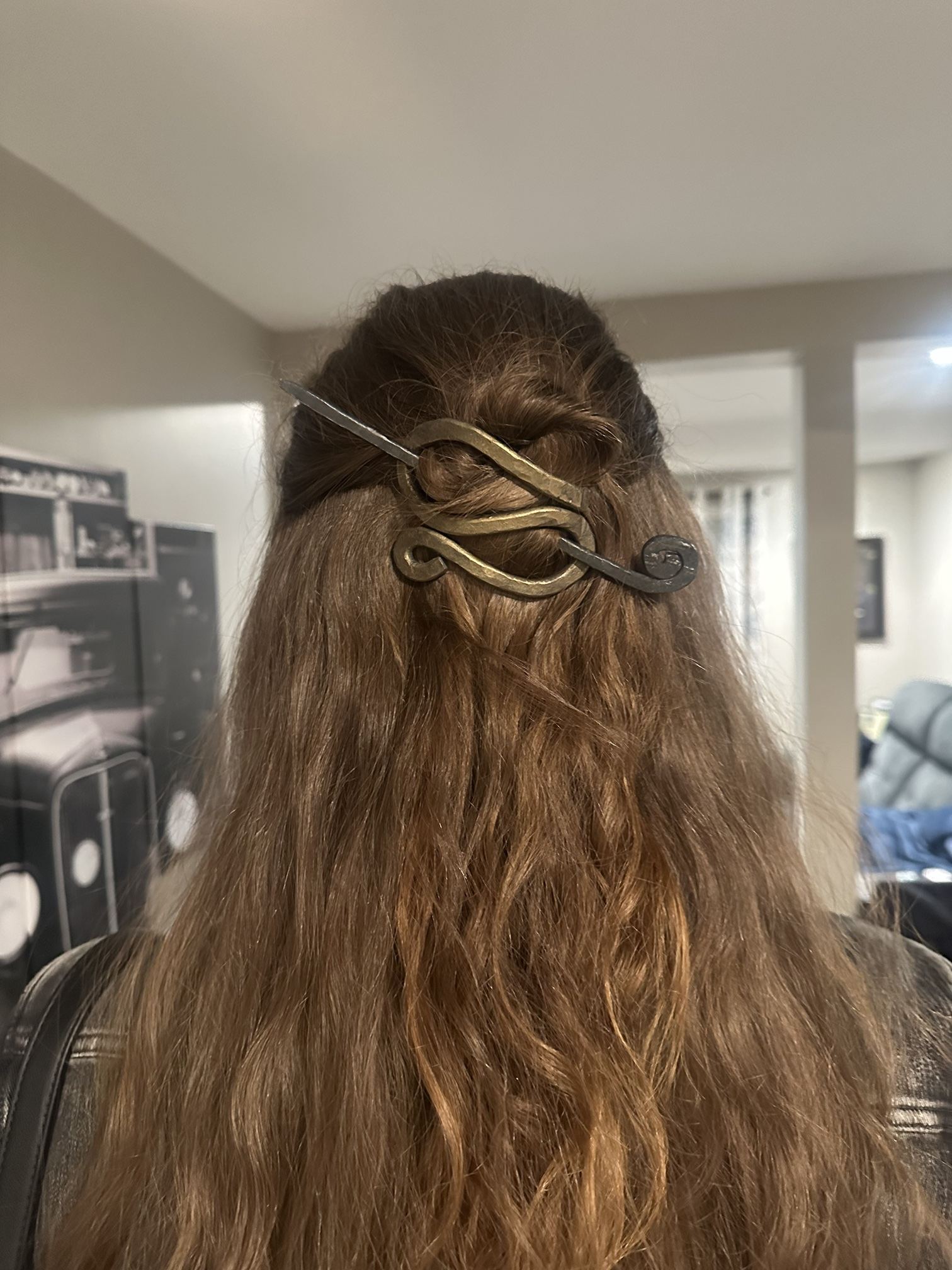 A forged hair slide with a scrolled pin holding a half-up bun in long hair.