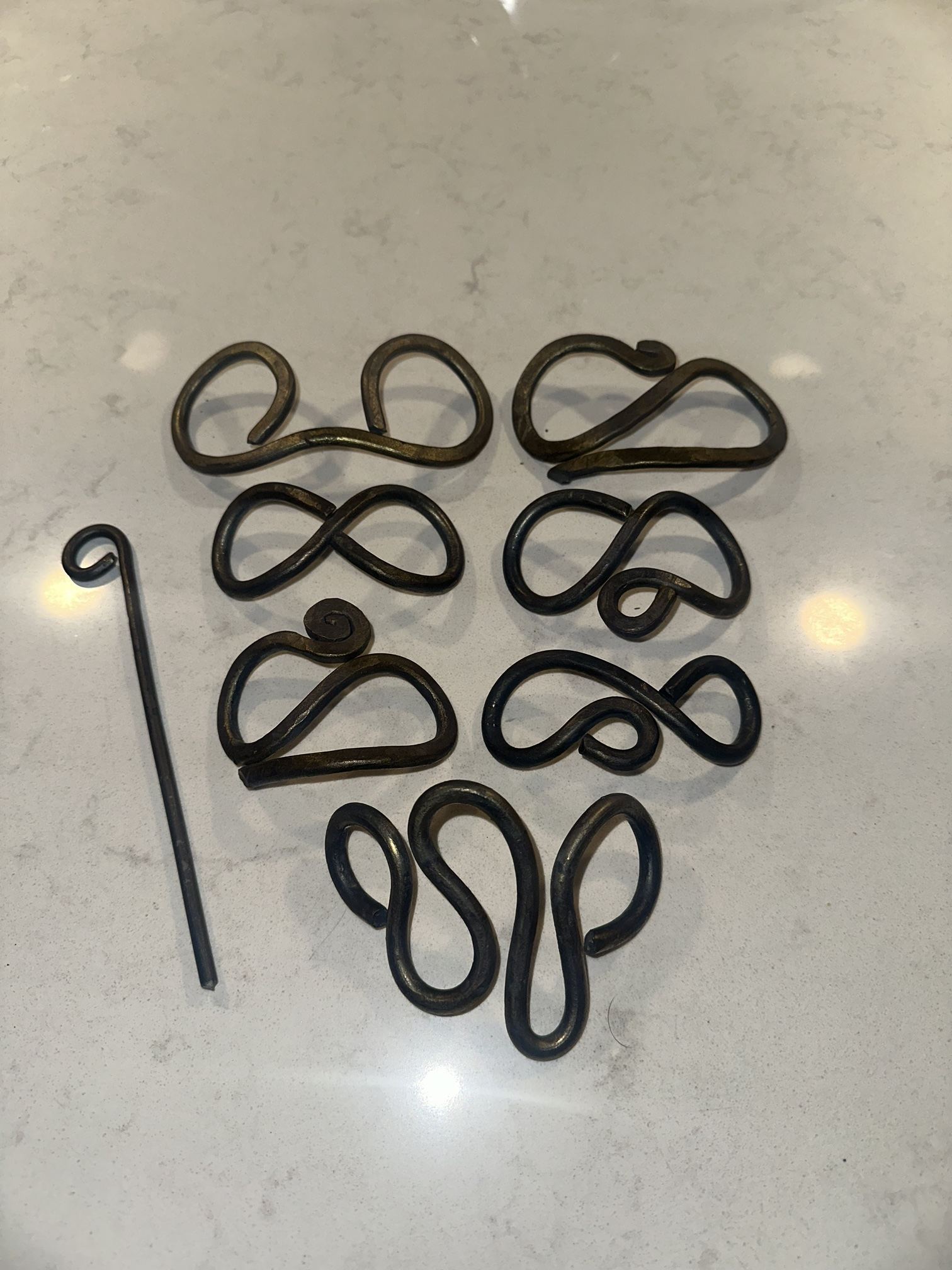 Seven hand-forged hair slides in different loop and scroll shapes, laid out beside a forged pin.