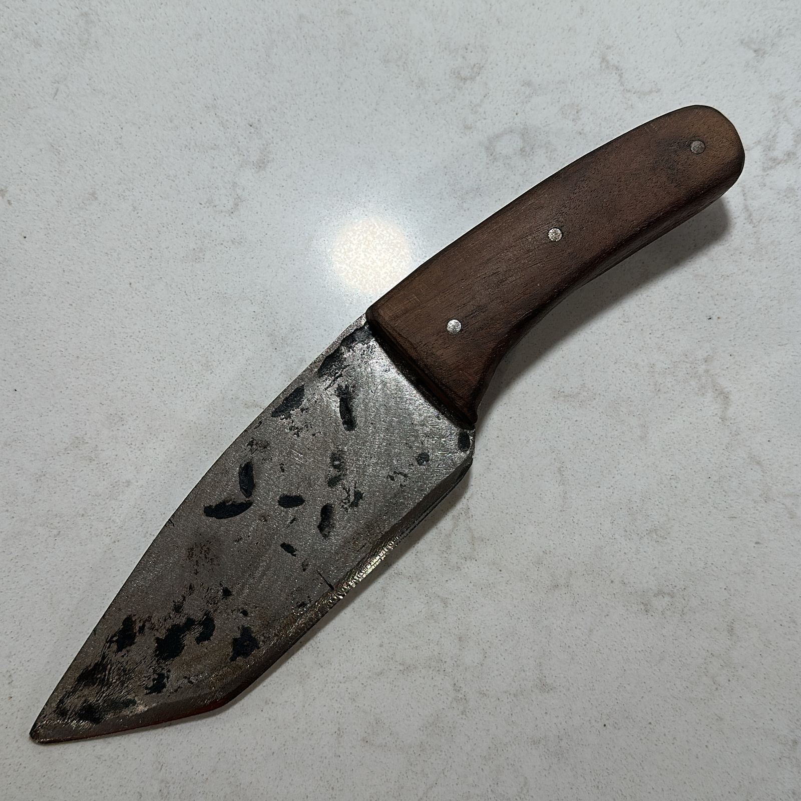 Hand-forged knife with an angled tip and mottled forge-finished blade, on a curved wooden handle with three pins.